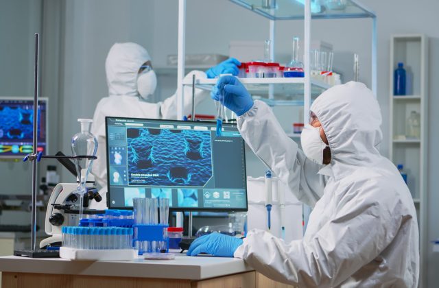 Neurologist with ppe suit working at vaccine development in equipped laboratory typing on pc. Team examining virus evolution using high tech for research in treatment development against covid19